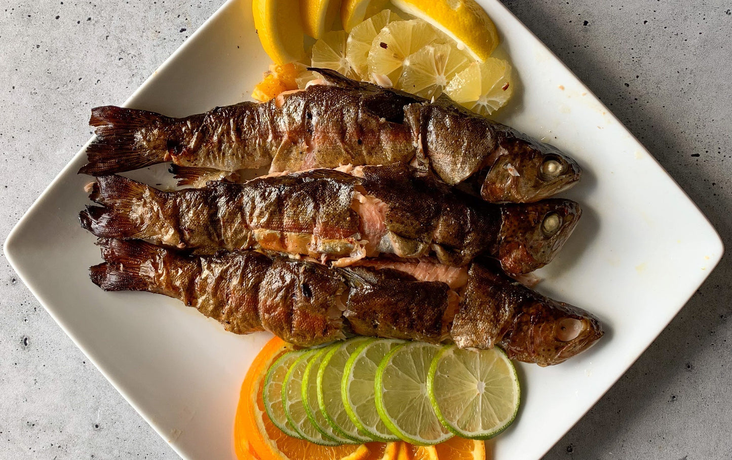 Smoked trout on a plate with orange, lemon, and lime slices